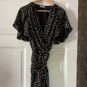 Valerie partklänning - Mycket fin kort festklänning från Valerie, svart med guldprickar, knyts omlott.  Använd ett fåtal gånger. Strl 40 men mer som en 38. 