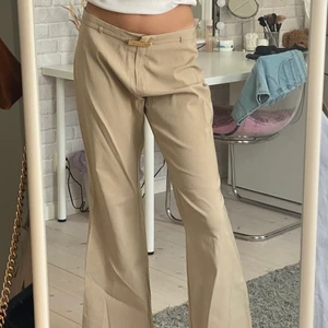 Beiga kostymbyxor  - Beiga lågmidjade kostymbyxor med ett tillhörande skärp. Är lite vida ner mot benet, fint skick!