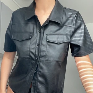 fejk läder/skinn blus - kortärmad skjorta i fejk skinn/läder med knappar. köpt secondhand men praktiskt taget i nyskick. 