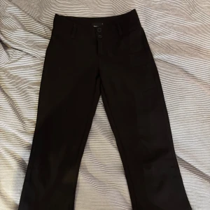 Gina y2k bootcut trousers  - Snygga svarta byxor från Gina Tricot i storlek XS. Byxorna har en klassisk design med knappar framtill och en ficka med knappdetalj bak. Perfekta för en stilren look.