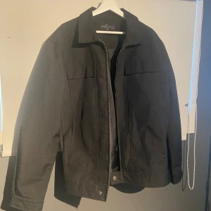 Svart jacka från Architects Style - Snygg svart jacka från Architects Style med dragkedja och fickor. Jackan har en klassisk krage och långa ärmar. Perfekt för en stilren look.                         Jackan är knappt använd och är i princip som ny.         Jackan är vattentålig och klarar regnskurar.                    Står L men passar också M