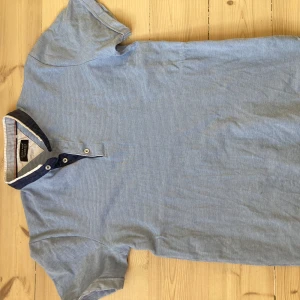 Blå randig pikétröja från Zara Man - Säljer en stilren blå randig pikétröja från Zara Man. Tröjan har korta ärmar och en klassisk krage med knappar. Perfekt för en avslappnad men snygg look. Passar bra till både jeans och chinos.