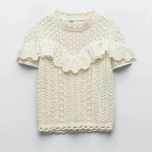 Vit stickad tröja med volangdetalj Zara - vit stickad tröja från Zara med en vacker volangdetalj över bröstet. Tröjan har korta ärmar och ett fint mönster. Storlek M.