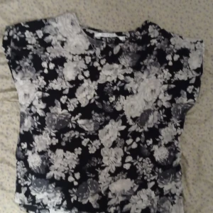 Svart och vit blommig blus från 157 Fabulous - Säljer en snygg svart och vit blommig blus från 157 Fabulous. Blusen har korta ärmar och ett vackert blommönster som ger en stilren look. Perfekt för att piffa upp garderoben! Skriv gärna om du vill ha mer information om blusen 