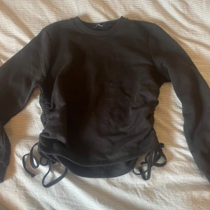 Svart tröja med snörning från Zara - Säljer en svart tröja från Zara med snörning i sidorna. Tröjan har långa ärmar och en rund halsringning. Perfekt för en stilren look. 