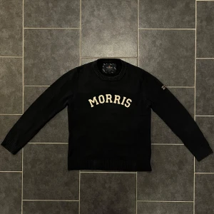 Svart tröja från Morris - Snygg svart tröja från Morris med vit text på bröstet. Tröjan har långa ärmar och en ribbad krage. Perfekt för en stilren look.