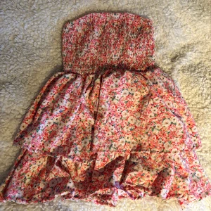 Blommig bandå klänning - Söt bandå klänning med blommigt mönster i rosa och vitt. Den har en smockad överdel och volangdetaljer på kjolen. Perfekt för sommarens varma dagar!