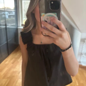 Svart ärmlös topp från Levate Room - Säljer en stilren svart ärmlös topp från Levate Room. Toppen har volangdetaljer vid axlarna och en lös passform. Perfekt för en chic och avslappnad look.