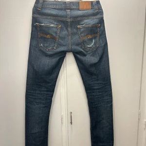 Faded raw denim jeans från Nudie - Snygga raw denim jeans från Nudie, med naturliga fades. Texten där modellen för byxorna står är tyvärr borttvättad, därmed vet jag inte modellen, men de sitter ungefär som grim Tim. Förutom de synliga slitningarna, så är jeansen i väldigt bra skick. Hör av dig vid intresse!