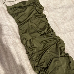 Olivgrön klänning med rynkdetaljer - Snygg olivgrön klänning med smala axelband och rynkdetaljer som ger en smickrande passform. Perfekt för en kväll ute eller en speciell tillställning. Använd en gång 