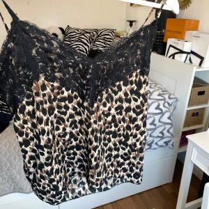 Leopardmönstrad linnetopp med spetsdetaljer - Snygg leopardmönstrad linnetopp med svarta spetsdetaljer vid halsringningen. Perfekt för en trendig look med tunna axelband och ett luftigt material.