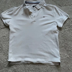 Vit pikétröja från Tommy Hilfiger - Säljer en klassisk vit pikétröja från Tommy Hilfiger. Tröjan har korta ärmar och en liten broderad logotyp på bröstet. Perfekt för en stilren och avslappnad look.