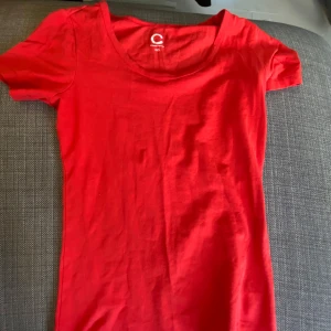Röd t-shirt i ekologisk bomull - Säljer en snygg röd t-shirt i ekologisk bomull från märket C. Den har en rund halsringning och korta ärmar, perfekt för en avslappnad stil. Passar utmärkt till både jeans och kjol. 🌟