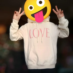 Beige hoodie med rosa text - Säljer en mysig beige hoodie med texten 'LOVE' i rosa på framsidan. Tröjan har en klassisk känguruficka och justerbar huva med dragsko. Perfekt för en avslappnad stil.