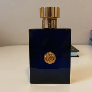 Blå parfymflaska från Versace - Elegant blå parfymflaska från Versace med en gyllene kork och ett ikoniskt guldemblem på framsidan. 100 ml flaska men ungefär 50 ml kvar