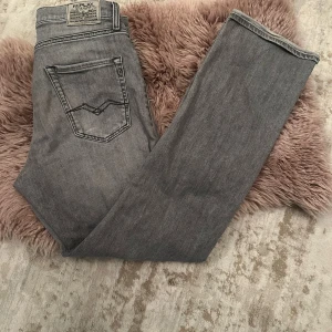 Grå jeans från Replay - Snygga grå jeans från Replay med klassisk femficksdesign. De har en rak passform och är perfekta för en avslappnad stil. Märkeslogga på baksidan och etikett inuti. Perfekta för dig som gillar stilrena och tidlösa plagg. 16 år.