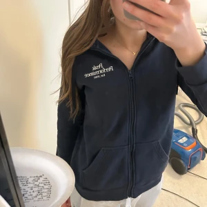 Zip hoodie - Säljer en mörkblå hoodie med dragkedja och text på bröstet. Perfekt för en avslappnad stil. Den har långa ärmar och en bekväm passform.