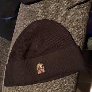 Svart mössa från Parajumpers - Snygg svart ribbad mössa från Parajumpers med broderad logga framtill. Perfekt för kyliga dagar och ger en stilren look. Passar både till vardags och mer avslappnade tillfällen.