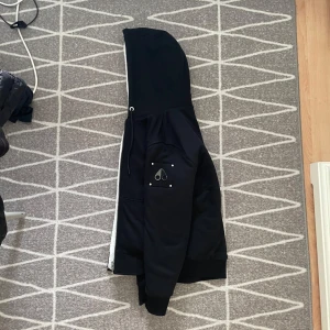 Svart jacka med huva från Moose Knuckles - Säljer en svart jacka med huva från Moose Knuckles. Jackan är köpt på Thernlunds I november och har anväts en del under vintern. Men är i riktigt gott skick nästan helt nytt. Kvitto finns på bild. Eller i verkligheten om man möts upp. Jackan funkar perfekt under höst och vår men även under dom kallare vintermånaderna. Nypris: 4599kr mittpris:2199. Hör av er vid funderingar, pris kan diskuteras vid snabb affär.     MVH Oscar :) 