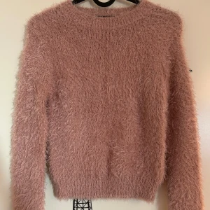 Rosa fluffig tröja från New Yorker  - Mysig rosa fluffig tröja med långärmad design från New Yorker i storlek XXS. Tröjan har en rund halsringning och en mjuk textur som ger en skön känsla. Använd ett väldigt fåtal gånger.