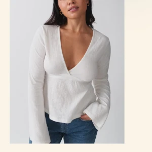 Vit omlottopp med knytband från Gina  - Säljer en stilren vit omlottopp med v-ringning och långa ärmar. Toppen har ett knytband i ryggen som ger en fin passform. Perfekt för en chic och avslappnad look. Har använt 3 gånger