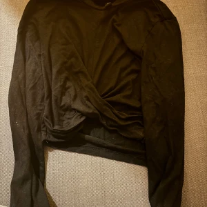 Svart långärmad topp från H&M - Säljer en svart långärmad topp från H&M med en snygg omlottdetalj framtill. Perfekt för en stilren look. 