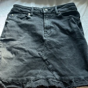 Svart jeanskjol - Snygg svart jeanskjol från IVY med en rå kant nertill och klassiska femficksdetaljer. Kjolen har en knapp och dragkedja framtill för enkel påklädning. Perfekt för en avslappnad stil.