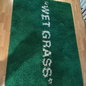 Grön matta med text från IKEA - Säljer en unik grön matta från IKEA designad av Virgil Abloh. Mattan har texten 'WET GRASS' i vitt och är en del av kollektionen 'Flooring' från 2019. Perfekt för att ge ditt rum en modern och konstnärlig touch.