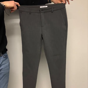 Grå kostymbyxor från Samsoe Samsoe - Snygga grå kostymbyxor från Oscar Jacobson med en elegant och stilren design. Byxorna har en normal passform och är tillverkade i ett fint material som ger en lyxig känsla. Perfekta för en formell look.