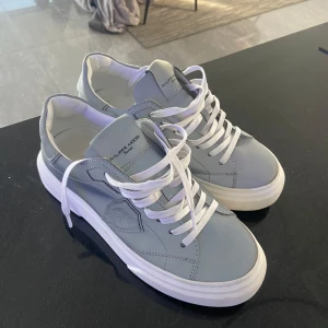 Grå sneakers från Philippe Model - Snygga grå sneakers från Philippe Model med vit sula och vita snören. Skorna har en stilren design med märkets logga på plösen.  Som nya