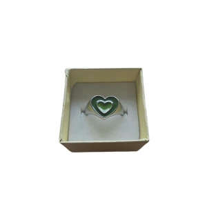 Silverring med grönt hjärta - Charmig silverring med ett grönt hjärta i mitten. Perfekt för att ge en färgklick till din stil. Ringen har en modern design med dubbla hjärtan i olika gröna nyanser. Okänt Material, US 6.5 eller 16.9 mm