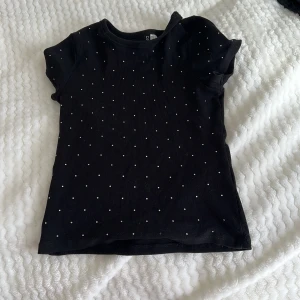 Svart ribbad topp från H&M Divided - Säljer en svart ribbad topp från H&M Divided med små vita prickar. Toppen har korta ärmar och en bekväm passform. Perfekt för en stilren look.❤️❤️