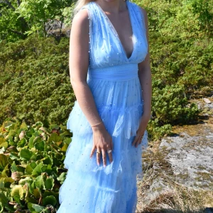 Ljusblå långklänning med volanger - Jag säljer min älskade balklänning för den förtjänar att förgylla någon annan än att hänga i min garderob! Den är endast använd en gång på min bal och är från fashion nova, men finns inte kvar på hemsidan. Den är i storlek S🩵