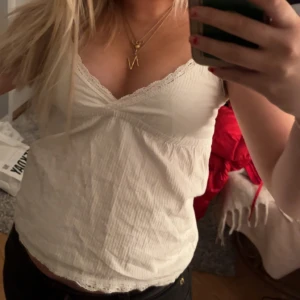 Vit linne med spetsdetaljer - Säljer ett sött vitt linne med spetsdetaljer och v-ringning. Perfekt för sommardagar eller som ett lager under en tröja. Linnet har en avslappnad passform och är tillverkat i ett lätt material.