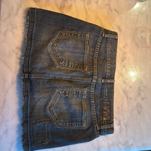 Jeanskjol från Converse - Snygg jeanskjol från Converse med slitna detaljer och fransad kant. Kjolen har klassiska femficksdesign och är perfekt för en avslappnad stil. Den är i en blå denimfärg och har en kort längd.