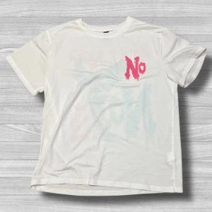 Vit t-shirt med tryck - Säljer en vit t-shirt med tryck. Framsidan har texten 'NO' i rosa och baksidan har texten 'TRUST NO ONE' i rosa och blått med en fågel. Perfekt för en avslappnad stil.