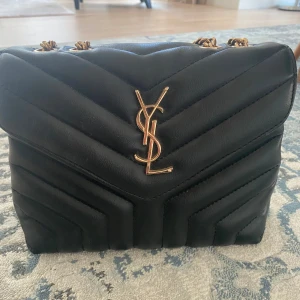 Svart quiltad axelväska från Saint Laurent - Snygg svart axelväska från Saint Laurent i quiltat skinn med guldfärgade detaljer. Väskan har en kedjerem. Perfekt för att ge en lyxig touch till din outfit.