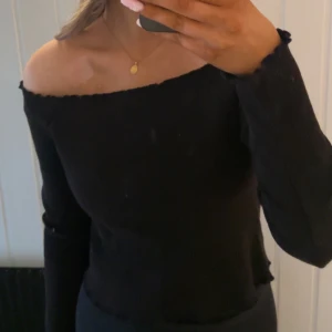 Svart offshoulder topp - Snygg svart offshoulder topp med långa ärmar. Perfekt för en stilren look. Toppen har en ribbad struktur som ger en fin detalj. (Står att den är i storlek L men skulle definitivt inte säga de, skulle säga S/M)