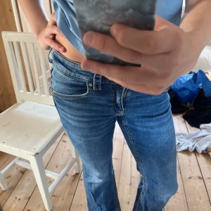 Blå jeans från Gina Tricot - Säljer ett par snygga blå jeans från Gina Tricot. De har en klassisk femficksdesign med en knapp och dragkedja framtill. Jeansen har en bootcut-stil som ger en skön retrovibe. Perfekta för en avslappnad look!