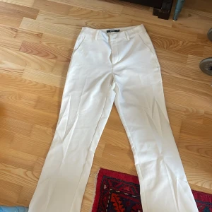 Vita kostymbyxor - Snygga vita kostymbyxor med en klassisk design. De har en rak passform och är perfekta för en stilren look. Byxorna har en dragkedja och knappar framtill.