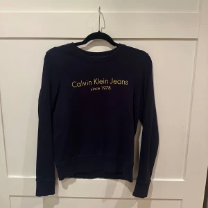 Mörkblå tröja från Calvin Klein Jeans - Marinblå Calvin Klein tröja i storlek S med gul text på bröstet. Använt sparsamt så väldigt fint skick💞