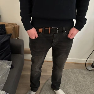 Svart flätat bälte med bruna detaljer - Snyggt svart flätat bälte med bruna läderdetaljer och silverfärgat spänne. Perfekt för att ge en stilren touch till din outfit. Passar till både jeans och chinos.