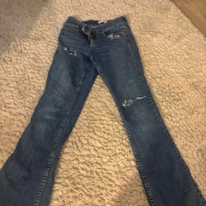 Blå jeans med slitningar - Snygga blå jeans med slitningar på låren och knäna. De har en klassisk femficksdesign och en bekväm passform. Perfekta för en avslappnad stil. Lågmidjade