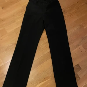 Svarta kostymbyxor från Lindex - Snygga svarta kostymbyxor från Lindex med en klassisk design. Byxorna har en knapp och dragkedja framtill samt hällor för bälte. Perfekta för en stilren look. Längden är för ca 165/168 🩷🩷