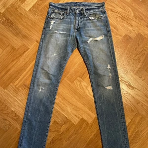 Blå distressed jeans från Ralph Lauren - Säljer ett par blå jeans från Ralph Lauren Denim & Supply med snygga slitningar detaljer framtill. Modellen har klassisk femficksdesign, rak passform och normal midja. Storlek 31:34