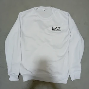 Vit EA7 sweatshirt -  Säljer snygg vit sweatshirt från EA7 Emporio Armani med svart logga på bröstet. Den är oanvänd, priset kan diskuteras vid snabb äffer.