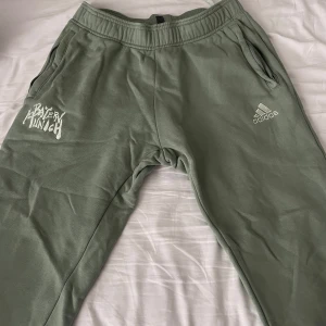 Adidas Bayern München mjukisbyxor - Gröna mjukisbyxor från Adidas med Bayern München-brodyr på ena benet. Byxorna har resår i midjan, snörning och dragkedjeförsedda fickor. Tillverkade i mjuk bomullsmix för skön känsla och avslappnad stil.