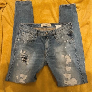Replay anbass 32/34 slitningar - Säljer ett par blå jeans från Anbass med en slim fit passform. De har en cool slitningseffekt på framsidan och klassiska femficksdetaljer. Perfekta för en avslappnad stil.