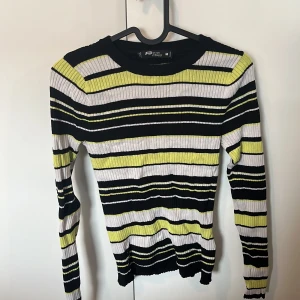 Randig ribbad tröja från FB Sister - Säljer en ribbad långärmad tröja från FB Sister i storlek M. Tröjan har ett randigt mönster i svart, vit och gul med figurnära passform. Perfekt för dig som gillar färg och vill sticka ut lite extra. Superenkel att styla till jeans eller kjol!