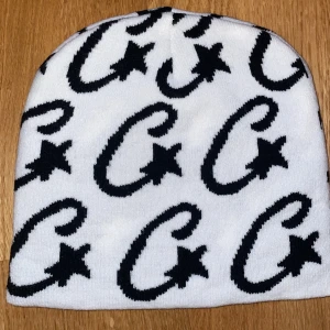 Vit mössa med svart stjärnmönster - Snygg vit mössa med svart grafiskt mönster av stora G:n och stjärnor över hela ytan. Mjuk och stretchig, perfekt för att hålla värmen och sticka ut i mängden. Passar dig som gillar streetstyle och vill ha en cool accessoar till vintern.